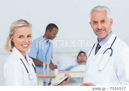 Smiling doctors standing in front of patient Smiling doctors standing in front of patient 7334317