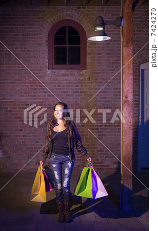 Mixed Race Young Woman Walking Carrying Shopping Bags at Night 7424279