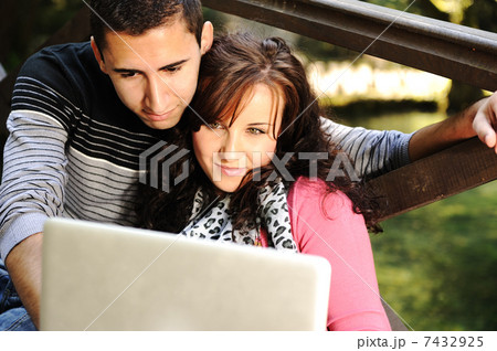 Young couple, male and female sitting in park and studing and workind together with notebook (laptop) 7432925