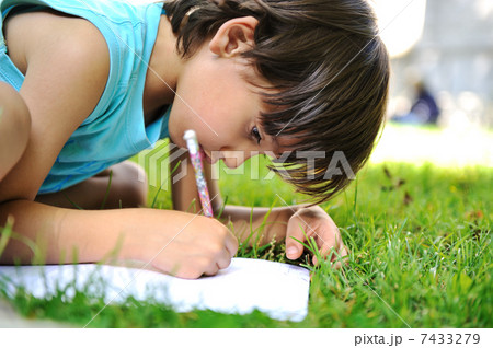 Young boy outdoors on the grass writing 7433279