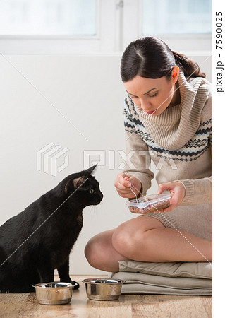 Beautiful young woman feeding her cat at home 7590025