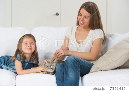 Mother and daughter sitting on sofa and cuddling cat Mother and daughter sitting on sofa and cuddling cat 7591412