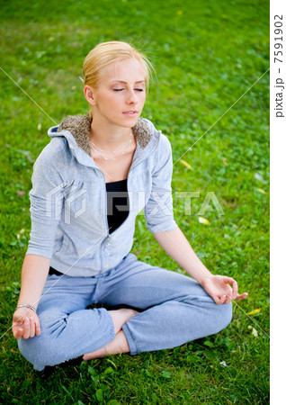Portrait of young woman meditating in pose of lotus on green gra 7591902