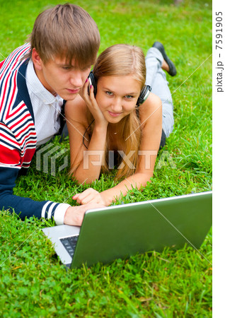 Happy young couple using laptop while lying on grass Happy young couple using laptop while lying on grass 7591905