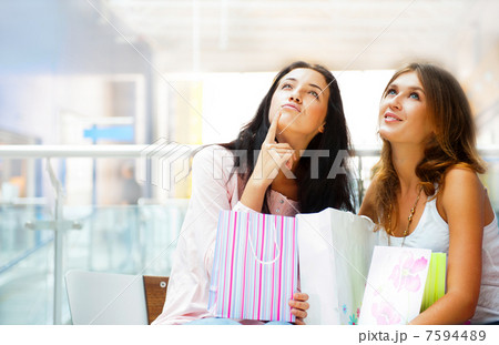 Two excited shopping woman resting on bench at shopping mall. Lo 7594489