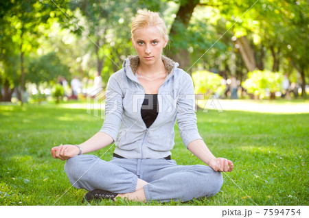 Portrait of young woman meditating in pose of lotus on green gra 7594754