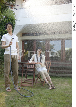 庭に水を撒く男性と見守る女性 7614677