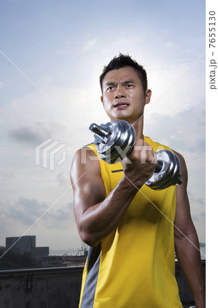 Athletic Young Chinese man exercising outdoors with dumbbells 7655130