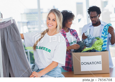 Cheerful volunteers putting clothes in clothes rail 7656708