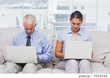 Business people sitting on sofa using their laptops 7659338