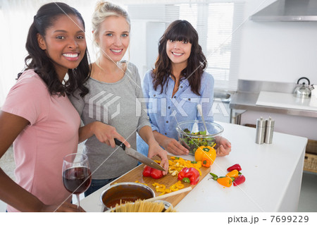 Cheerful friends preparing a meal together looking at camera 7699229