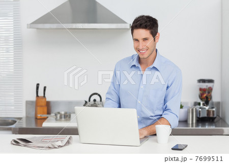 Portrait of a man using a laptop in the kitchen Portrait of a man using a laptop in the kitchen 7699511