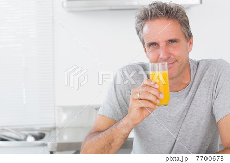 Smiling man having glass of orange juice in kitchen 7700673