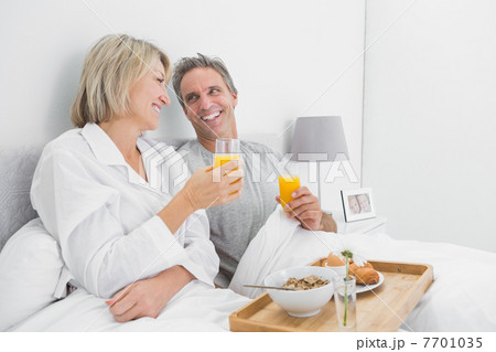 Cheerful couple having orange juice at breakfast in bed Cheerful couple having orange juice at breakfast in bed 7701035