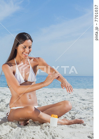 Smiling woman sitting on beach applying sunscreen Smiling woman sitting on beach applying sunscreen 7701037