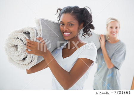 Happy housemates carrying rolled up rug 7701361