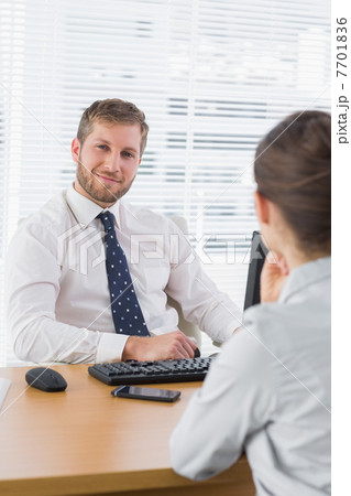 Businessman smiling with a co worker sitting at his desk 7701836
