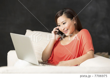 Chinese woman sitting on sofa using laptop and talking on phone. 7706975