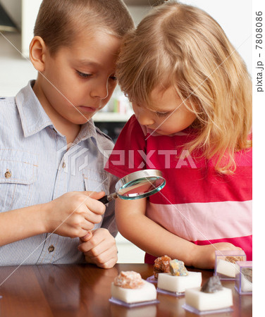 Children are considering a magnifying glass collection of stones 7808086