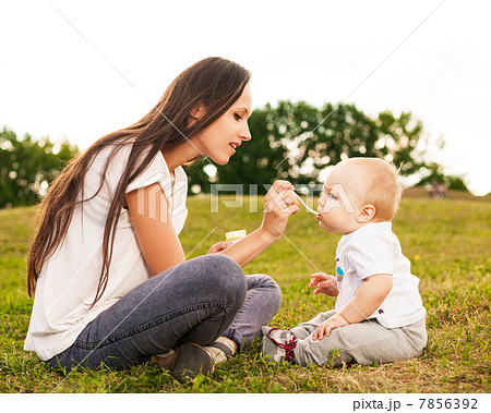 Young beautiful mother feeding her baby puree outdoors in sunlight 7856392