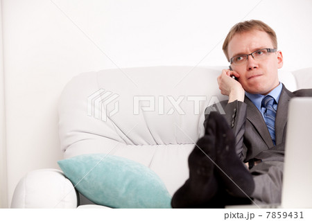 Good-looking young man seated on the sofa and talking at cellphone 7859431