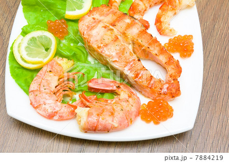 a piece of broiled fish, shrimp and red caviar on white plate cl 7884219