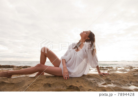 Young woman wearing white top sitting on sand, portrait Young woman wearing white top sitting on sand, portrait 7894428