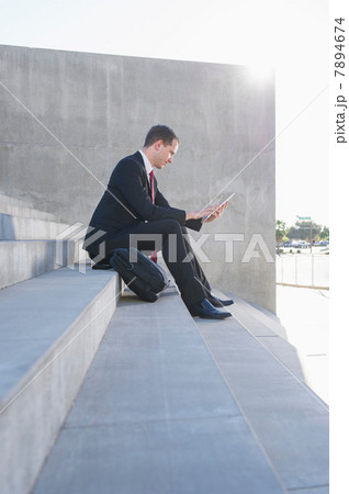 Businessman sitting on concrete steps using digital tablet Businessman sitting on concrete steps using digital tablet 7894674