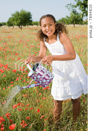 Young girl watering poppy field with watering can Young girl watering poppy field with watering can 7894810