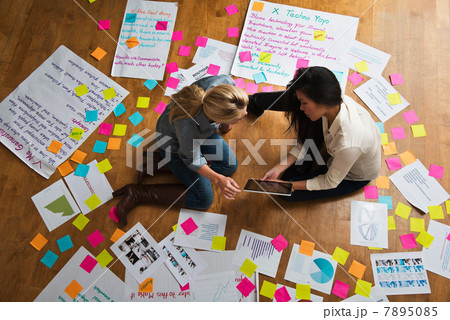 Colleagues sitting on floor with digital tablet, papers and adhesive notes Colleagues sitting on floor with digital tablet, papers and adhesive notes 7895085
