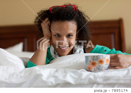 Young woman lying on bed holding tea cup Young woman lying on bed holding tea cup 7895174