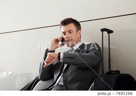 Businessman on cell phone waiting with luggage and checking watch 7895266