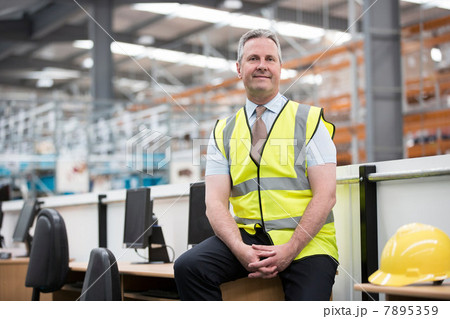 Man sitting on desk in warehouse, portrait 7895359