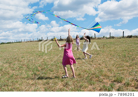 Three girls flying kite in field 7896201