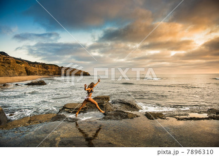 Young woman in bikini leaping from rocks on beach Young woman in bikini leaping from rocks on beach 7896310