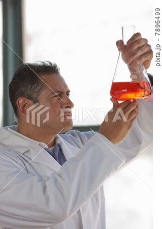Mature scientist looking at liquid in volumetric flask 7896499