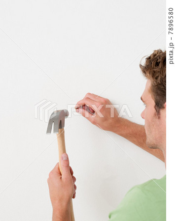 Young man hammering nail into wall 7896580