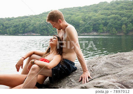 Couple sitting together on rock at lakeside 7897012