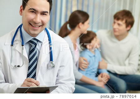 Doctor looking at camera and smiling with a family in the background Doctor looking at camera and smiling with a family in the background 7897014