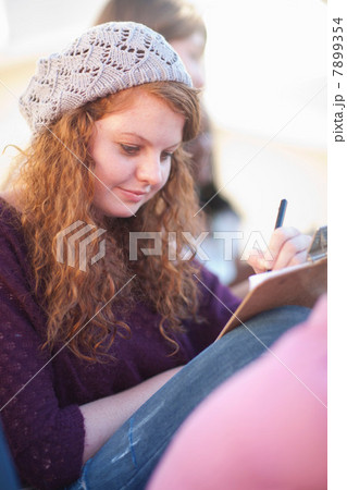 Young woman wearing knit hat writing on clipboard Young woman wearing knit hat writing on clipboard 7899354
