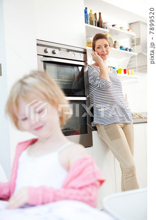 Mother on cell phone in kitchen with daughter in foreground Mother on cell phone in kitchen with daughter in foreground 7899520