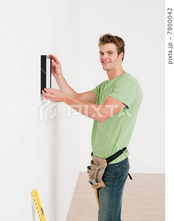 Young man hanging picture on wall Young man hanging picture on wall 7900042