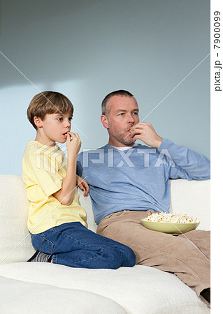 Father and son watching television eating popcorn Father and son watching television eating popcorn 7900099