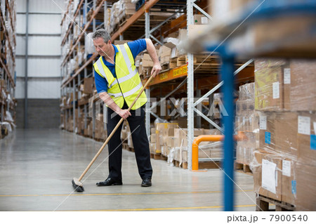 Man sweeping warehouse floor with broom 7900540