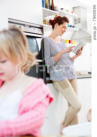Mother using digital tablet, daughter in foreground 7900690