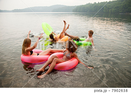 Friends playing in inflatable rings on lake 7902638