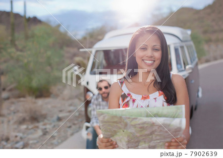 Young woman holding map on road trip, smiling 7902639