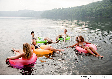 Friends playing in inflatable rings on lake 7903479