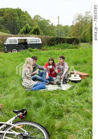 Friends sitting in field by camper van 7903595