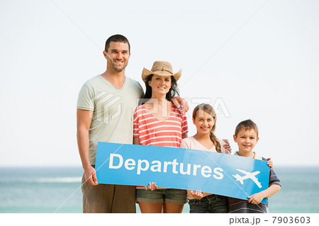Family holding an airport departures sign on a beach 7903603